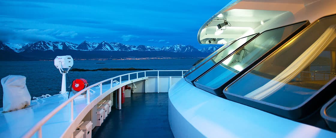 Vue panoramique d'un luxueux bateau de croisière TMR Croisières, naviguant vers des paysages montagneux majestueux.